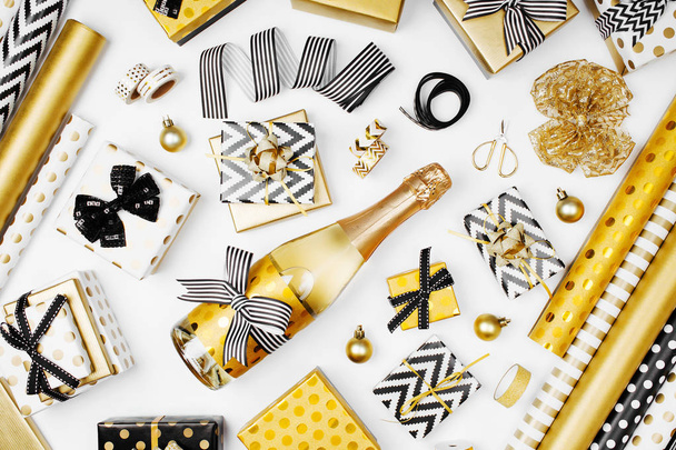 flat lay of champagne bottle, presents and golden wrapping paper rolls on white background - Valokuva, kuva