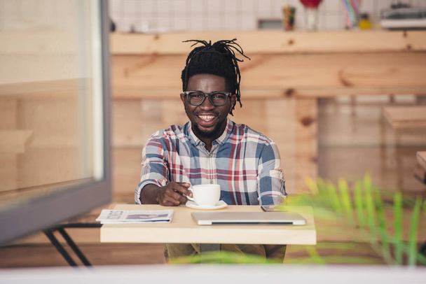 fröhlicher afrikanisch-amerikanischer Mann trinkt Kaffee am Tisch im Café - Foto, Bild