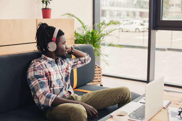 Afrikanisch-amerikanischer Mann hört Musik mit Kopfhörern im Café mit Laptop - Foto, Bild