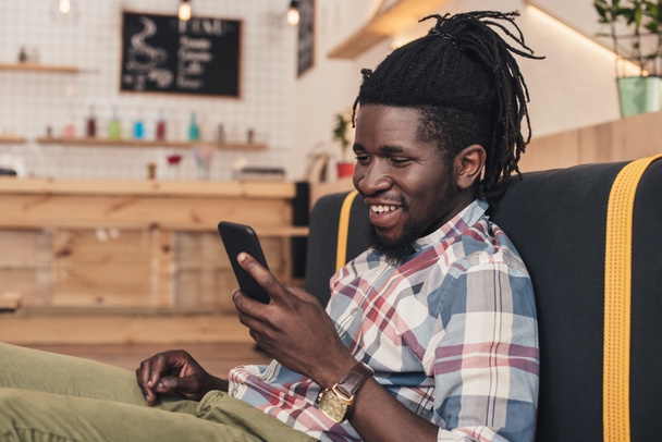 smiling african american man using smartphone in cafe - Foto, afbeelding