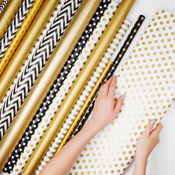 female hands holding set of wrapping paper rolls in golden colors - Foto, afbeelding