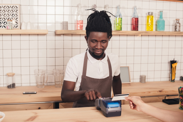 barista afroamericano con lector de tarjetas de crédito en mostrador de bar
 - Foto, Imagen