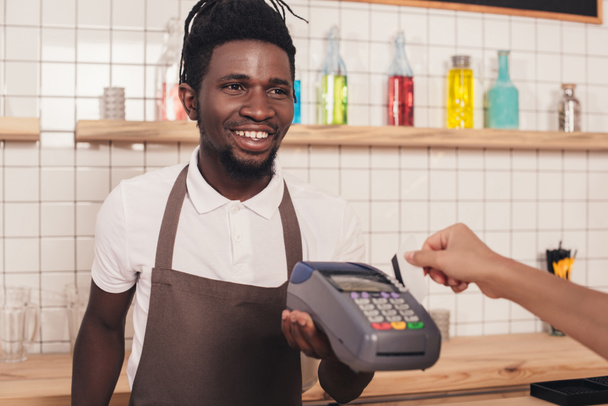Бариста держит терминал, пока клиент платит кредитной картой в кафе
 - Фото, изображение