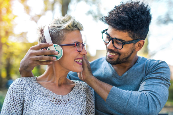 joven pareja de raza mixta escuchando música a través de auriculares al aire libre
 - Foto, Imagen