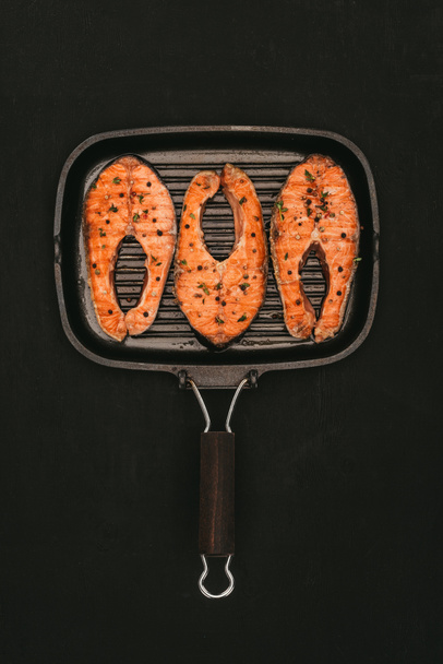 top view of grill with delicious salmon steaks isolated on black - Fotoğraf, Görsel