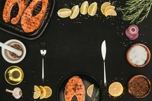 top view of grilled salmon steaks, cutlery and spices on black - Photo, Image