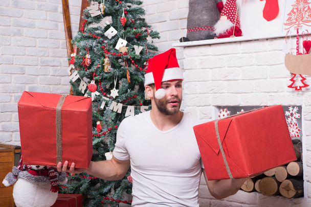 Macho in santa hat hold wrapped gifts at fireplace - Photo, image