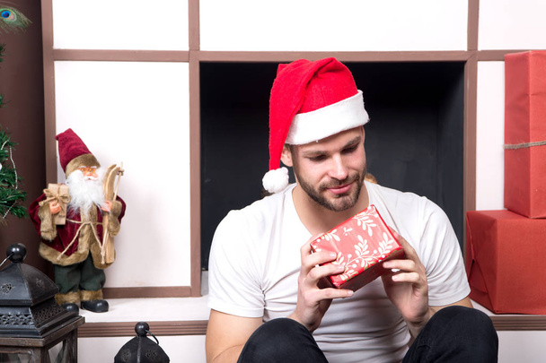 Man in santa hat look at red box at fireplace - Foto, Bild