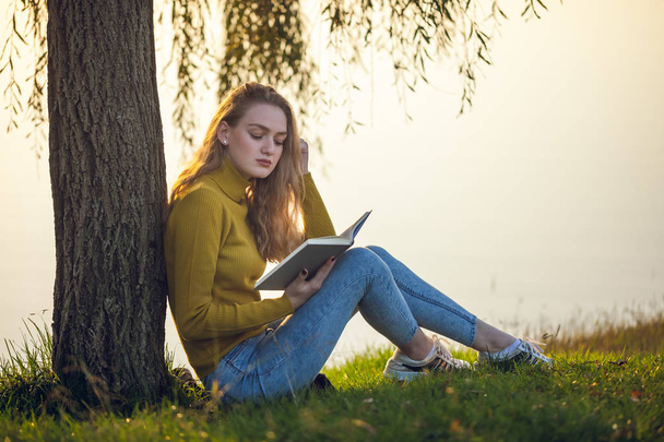 Mooie jonge blonde vrouw zitten en lezen boek in een park  - Foto, afbeelding