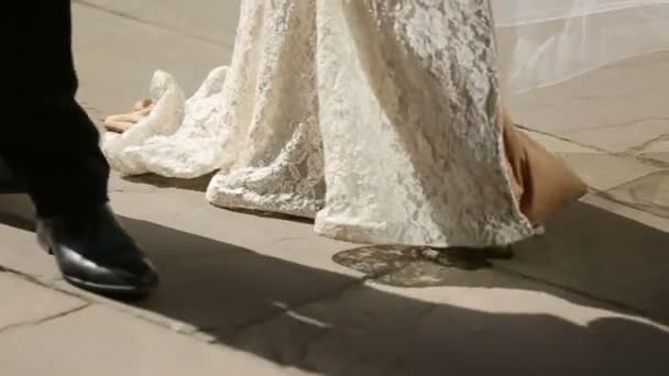 Γαμπρός και νύφη στο φόρεμα από δαντέλα με τα πόδια στις ακτίνες του ήλιου το πρωί - Πλάνα, βίντεο