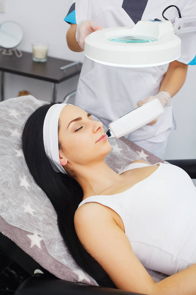 Cosmetologie. Ultrasone gezicht reinigen, peeling, in een schoonheidssalon. Mooie vrouw ontvangen gezichtshuid ultrasone cavitatie. - Foto, afbeelding