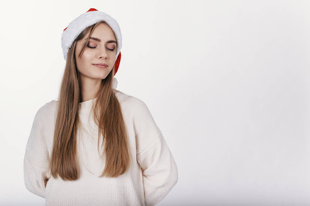 Woman in santa hat close her eyes and start to dreaming about her holidays and gifts - Photo, Image