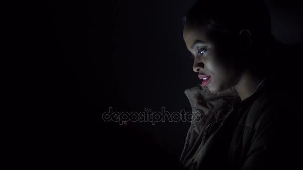 Musta nainen lukee jotain hänen iPhone seisoo pimeydessä
 - Materiaali, video
