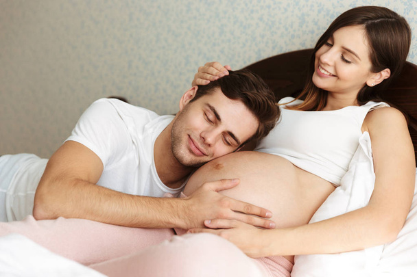 Smiling young pregnant wife lying in bed with her husband - Fotoğraf, Görsel