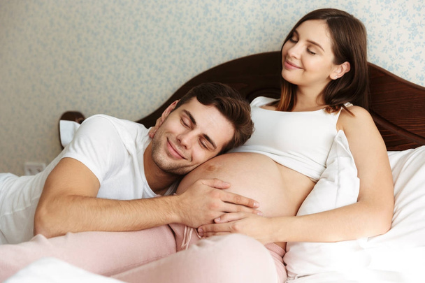 Delighted young pregnant wife lying in bed - Photo, Image