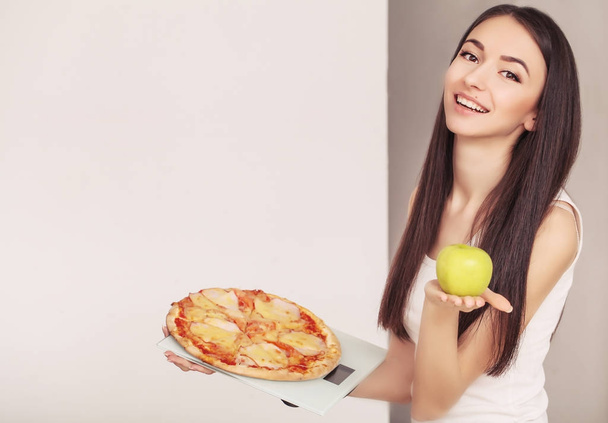 Dieet. Een jonge vrouw die houdt van een pizza op de weegschaal. Het begrip van gezond eten - Foto, afbeelding