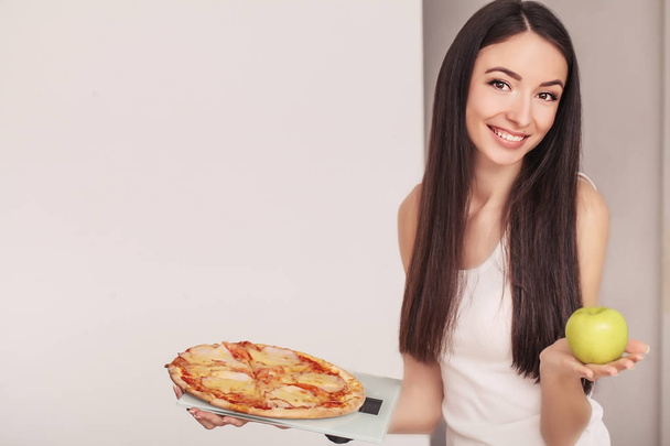 Diet. A young woman holding a pizza on the scales. The concept of healthy eating - Photo, Image