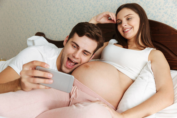 Joyful young pregnant couple taking selfie - Foto, afbeelding