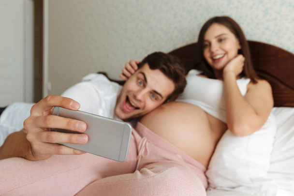 Cheerful young pregnant couple taking selfie - Фото, зображення