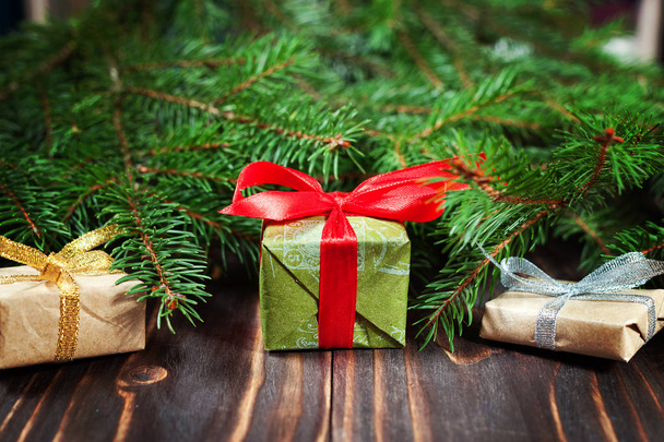 Рождественские подарки с красной лентой на деревянном фоне в рамке из еловых ветвей
. - Фото, изображение