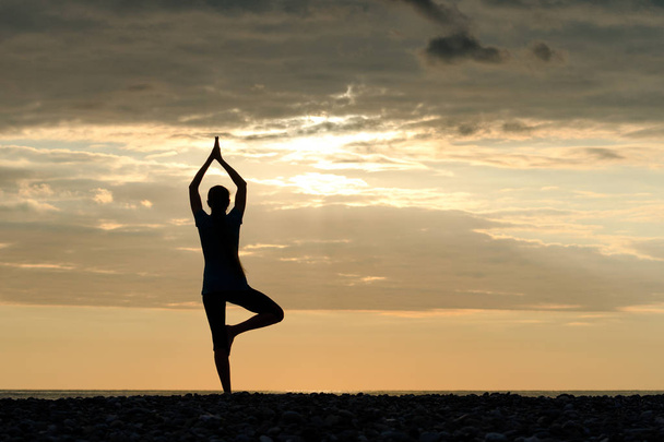 Fille au coucher du soleil pratiquant le yoga au bord de la mer, silhouette
 - Photo, image