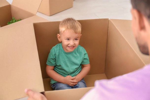 Cute little boy sitting in moving box and playing with his father at home - 写真・画像