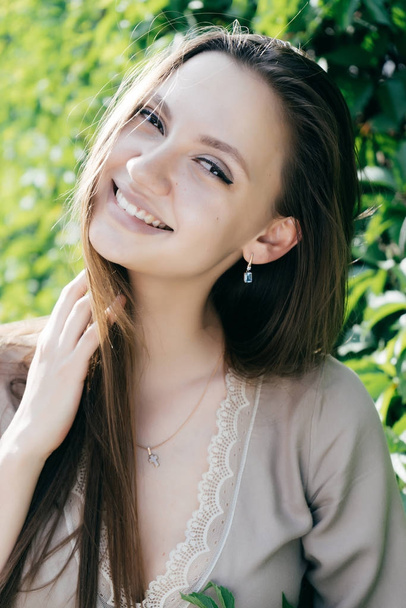 cheerful girl smiles widely and looks directly at the camera on a background of green leaves - 写真・画像
