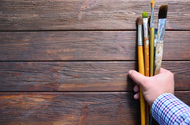 Wooden background with a hand of an artist with brushes. - Foto, imagen