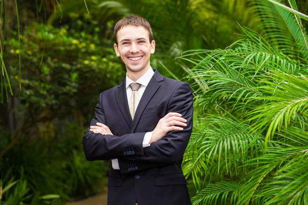 Heureux homme d'affaires souriant en costume d'affaires dans le jardin de palmiers. Harmonie avec la nature. Concept d'un succès
  - Photo, image