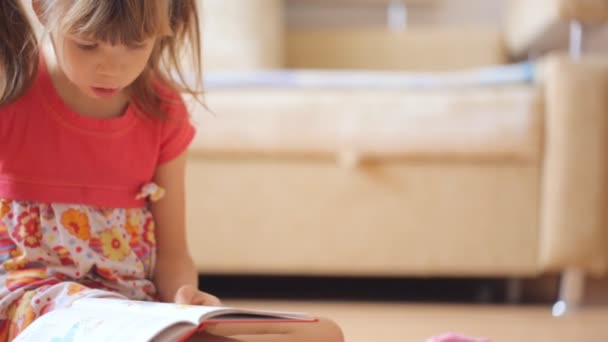 Pikkutyttö lukee kirjaa lattialla.
 - Materiaali, video