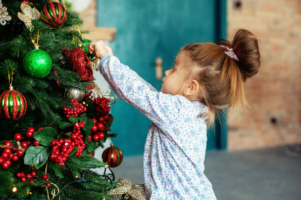 Egy kislány díszíti a karácsonyfát.  - Fotó, kép