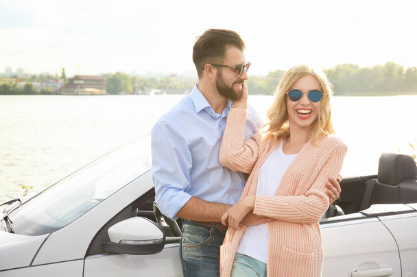 Happy young couple standing near car on river bank - Φωτογραφία, εικόνα