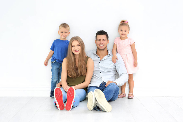 Szczęśliwa rodzina siedzi na podłodze w pobliżu biała ściana w nowym domu - Zdjęcie, obraz