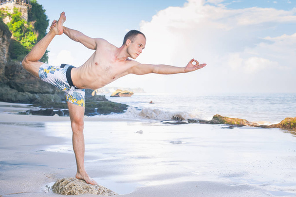 Handsome man doing yoga at cliff with blue sea background - Fotó, kép