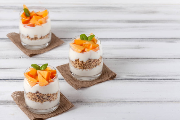 Persimmon creamy trifle in beautiful glasses, fresh ripe fruit slices on white wooden background. Healthy vegetarian food. Delicious dessert. Close up photography. Selective focus. - Photo, Image
