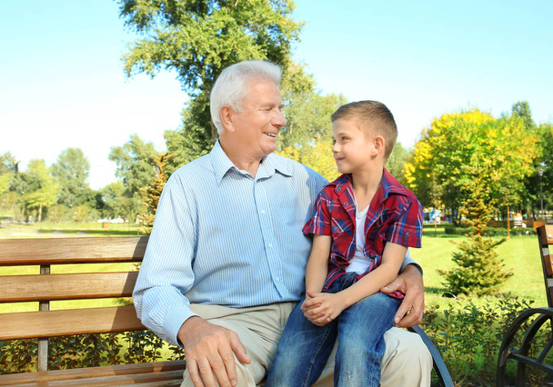 Пожилой человек с внуком сидит на скамейке в парке
 - Фото, изображение