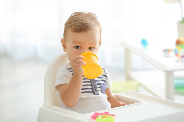Adorable baby drinking from bottle while sitting in highchair at home - Foto, Imagen