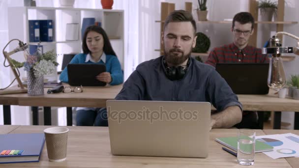Stressed man working at desk in creative office - Footage, Video