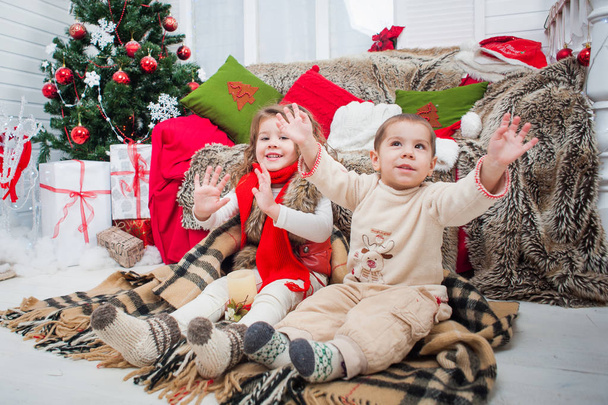 Pikkupoika ja tyttö istumassa matolla lähellä joulukuusta
. - Valokuva, kuva