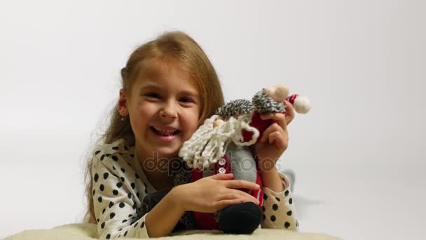 Portrait of happy girl hugging Santa claus toy. Funny young girl waving hello - Metraje, vídeo