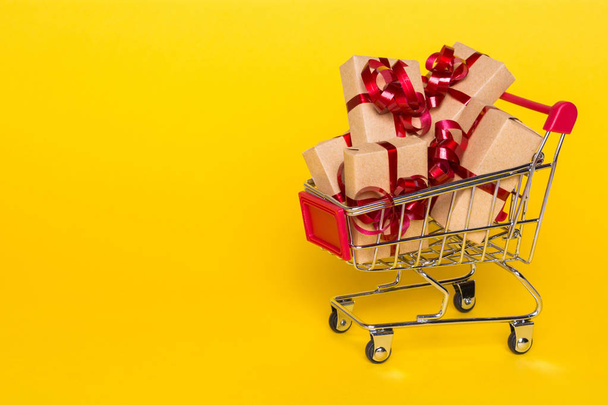 Creative concept with shopping trolley with gifts on a yellow background - Photo, Image