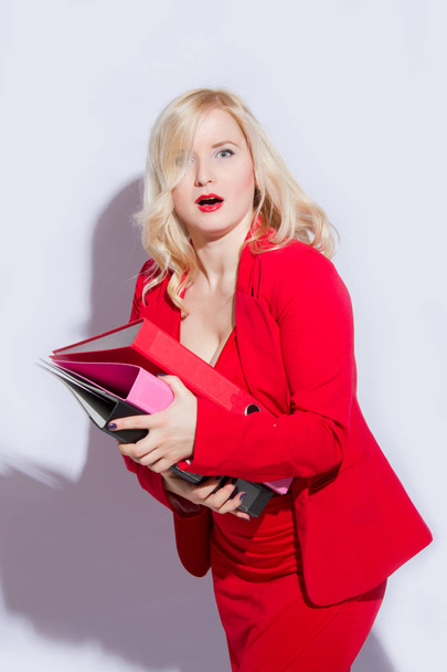Portrait of a beautiful young blonde woman in a red business suit. The girl holds a folder for documents - Foto, afbeelding