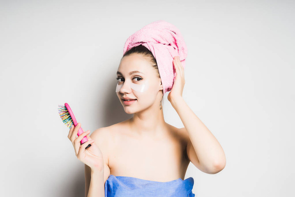 cheerful girl after shower with pink towel on her head holds a comb in her hands and looks into the camera, isolated - Фото, зображення