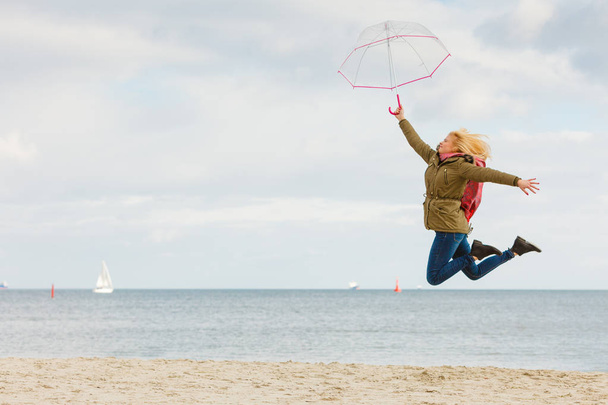 Frau springt mit durchsichtigem Regenschirm am Strand - Foto, Bild