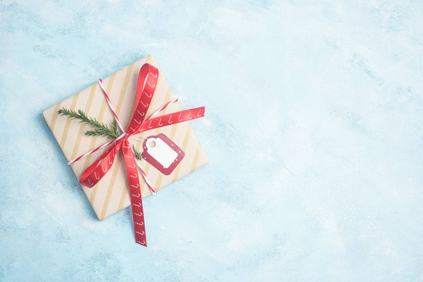 Flat lay top view christmas gift box wrapped in craft paper with red ribbon on light blue background. New year concept. Text space - Fotoğraf, Görsel