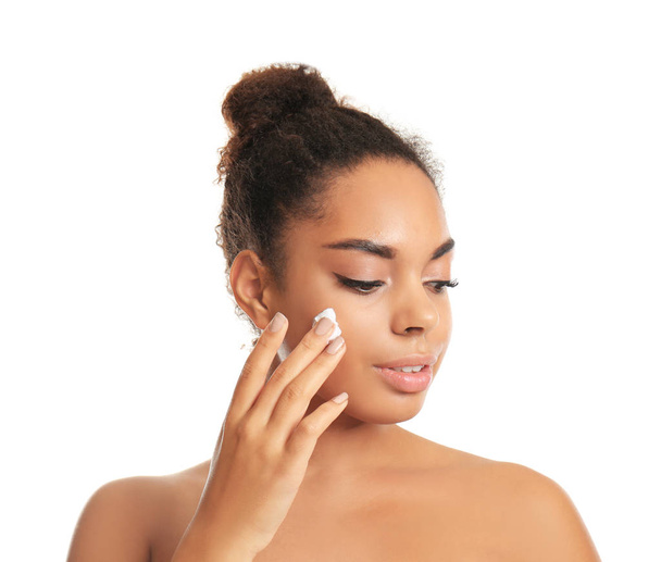 Beautiful young African American woman applying cream onto skin on white background - 写真・画像