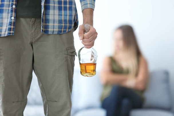 Man with bottle of alcohol and blurred woman - Foto, imagen