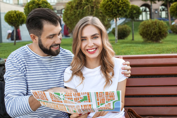 Couple of young tourists with map sitting on bench outdoors - Fotografie, Obrázek