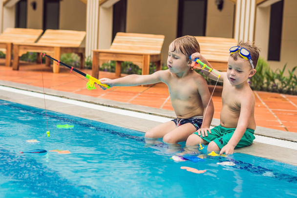 Two little cute boys catching a toy fish in the pool - Fotó, kép