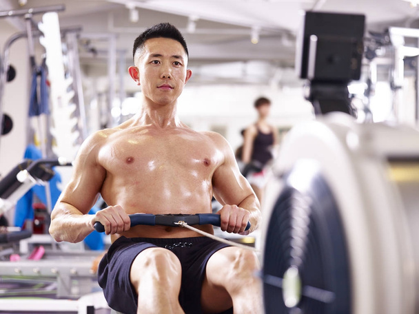 junger asiatischer Mann trainiert mit Rudergerät - Foto, Bild